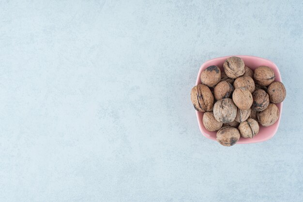 Un pequeño plato rosa lleno de nueces sobre fondo de mármol. Foto de alta calidad