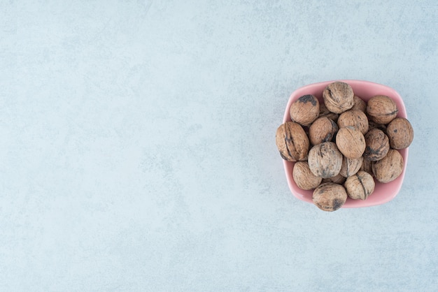 Un pequeño plato rosa lleno de nueces sobre fondo de mármol. Foto de alta calidad