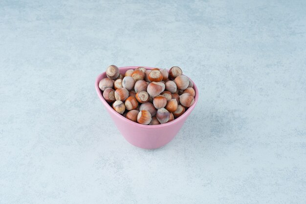 Un pequeño plato rosa lleno de nueces sobre fondo de mármol. Foto de alta calidad