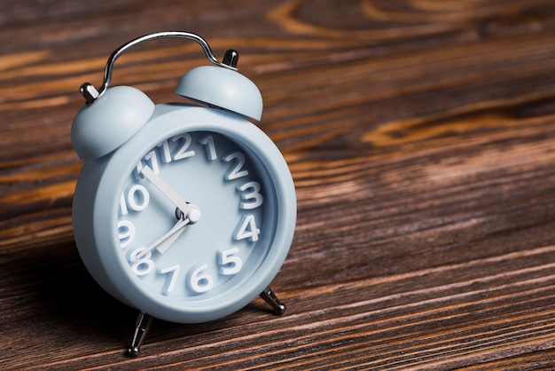 Pequeño reloj despertador azul sobre fondo de madera con textura