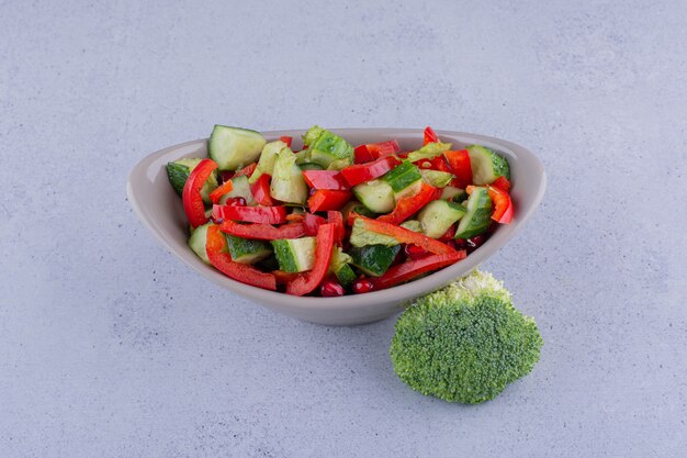 Pequeño tazón de ensalada junto a un trozo de brócoli sobre fondo de mármol. Foto de alta calidad