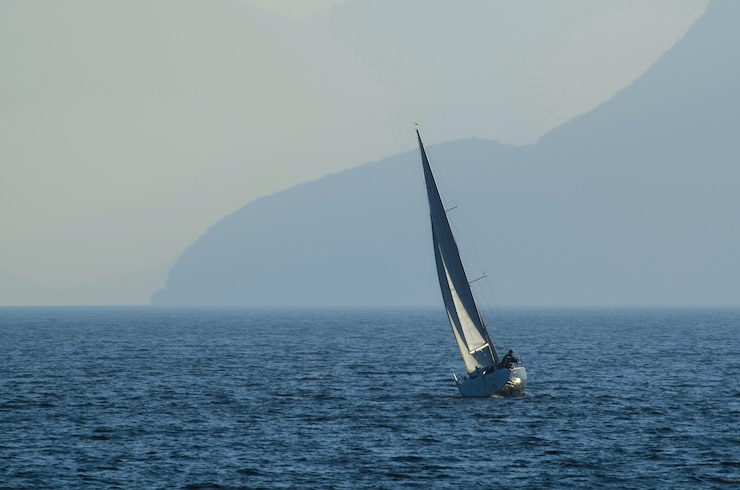 Foto gratuito pequeño velero en el mar rodeado de montañas cubiertas de niebla durante el día