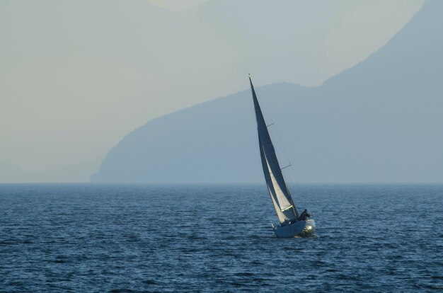 Pequeño velero en el mar rodeado de montañas cubiertas de niebla durante el día