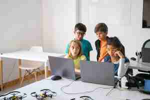 Foto gratuita pequeños compañeros de clase haciendo tareas grupales, usando computadoras portátiles y estudiando en la escuela de informática