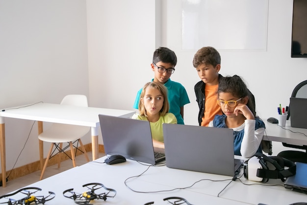 Pequeños compañeros de clase haciendo tareas grupales, usando computadoras portátiles y estudiando en la escuela de informática
