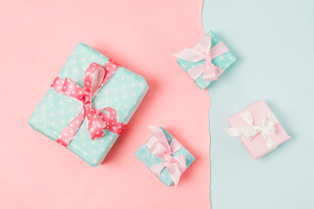 Pequeños y grandes regalos decorados en caja, atados con cinta, en papel tapiz azul y melocotón.