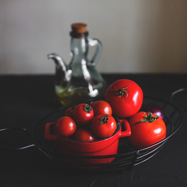 Pequeños y grandes tomates maduros en jarrón de acero y maceta de cerámica roja