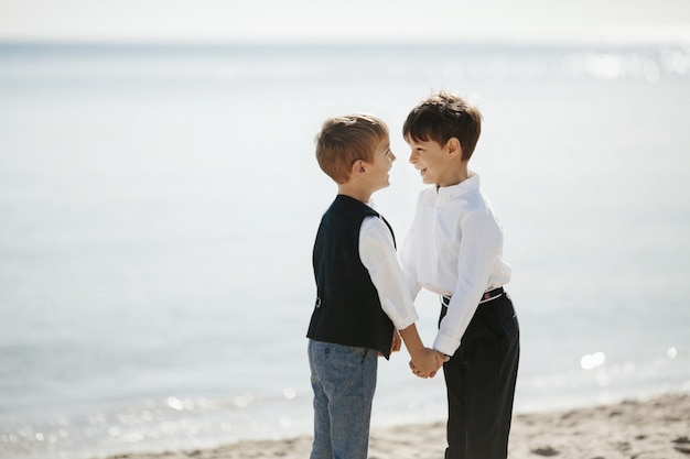 Pequeños hermanos sonrientes están tomados de la mano en el día soleado en la costa del océano