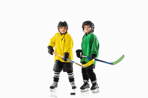 Pequeños jugadores de hockey con los palos en la cancha de hielo y fondo blanco.
