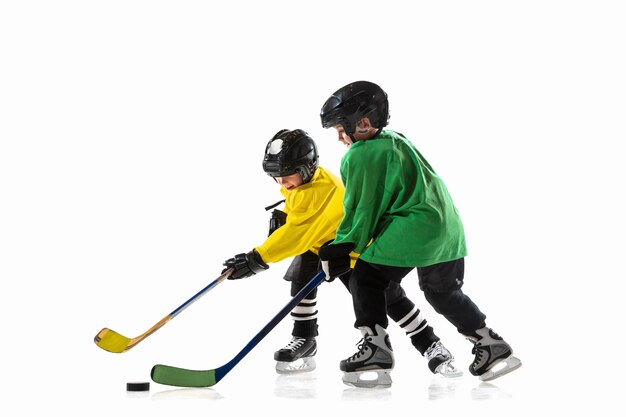 Pequeños jugadores de hockey con los palos en la cancha de hielo y pared blanca. Deportistas con equipo y casco practicando. Concepto de deporte, estilo de vida saludable, movimiento, movimiento, acción.