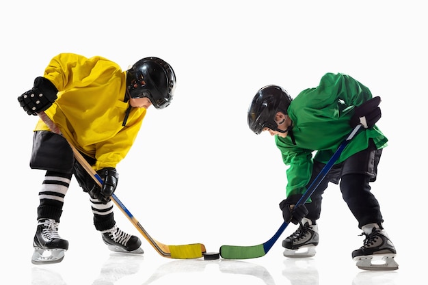 Pequeños jugadores de hockey con los palos en la cancha de hielo y pared blanca. Deportistas con equipo y casco practicando. Concepto de deporte, estilo de vida saludable, movimiento, movimiento, acción.