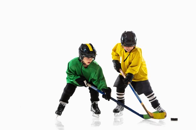 Pequeños jugadores de hockey con los palos en la cancha de hielo y pared blanca. Deportistas con equipo y casco practicando. Concepto de deporte, estilo de vida saludable, movimiento, movimiento, acción.