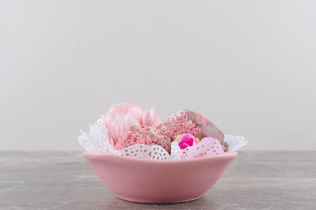 Foto gratuita pequeños pasteles y corolas de flores en un cuenco cubierto de tapete sobre mármol