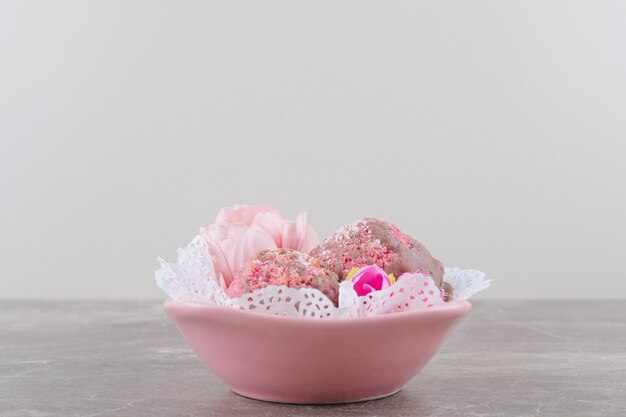 Pequeños pasteles y corolas de flores en un cuenco cubierto de tapete sobre mármol