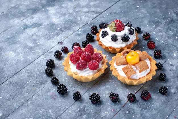 Foto gratuita pequeños pasteles cremosos con frambuesas junto con moras en forma de corazón en un escritorio luminoso, bizcocho de frutas y bayas