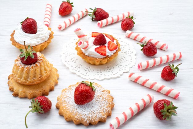 Pequeños pasteles deliciosos con crema y fresas en rodajas dulces en blanco, pastel de baya dulce azúcar hornear