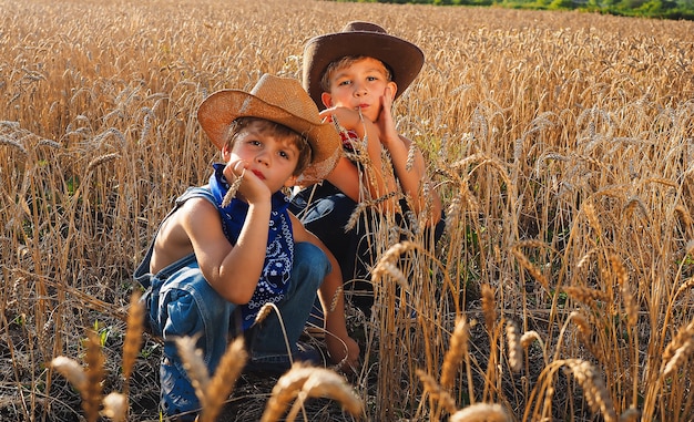 Pequeños vaqueros adorables sentados en un campo de trigo durante el día