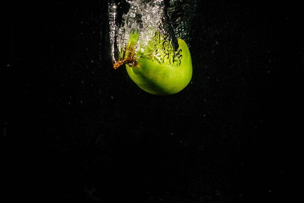 Pera verde cae en el agua sobre fondo negro