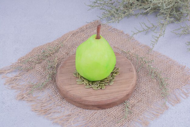 Una pera verde sobre una tabla de madera con semillas de calabaza