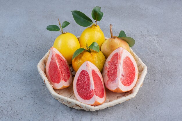 Foto gratuita peras y rodajas de pomelo en una canasta blanca sobre fondo de mármol.