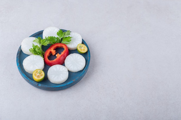 Perejil picado, rábano, pimienta, kumquat en placa de madera sobre mesa de mármol.
