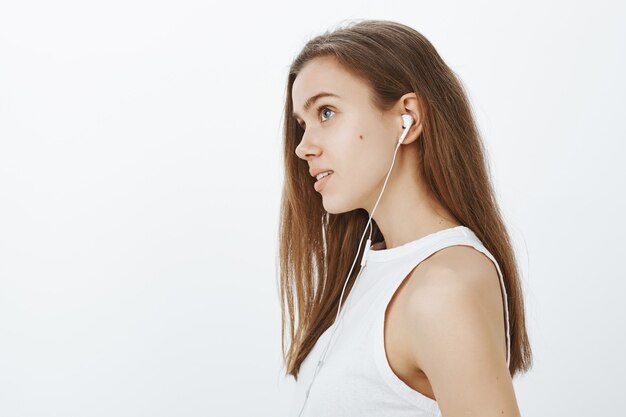 Perfil de chica atractiva soñadora escuchando podcast o música en auriculares