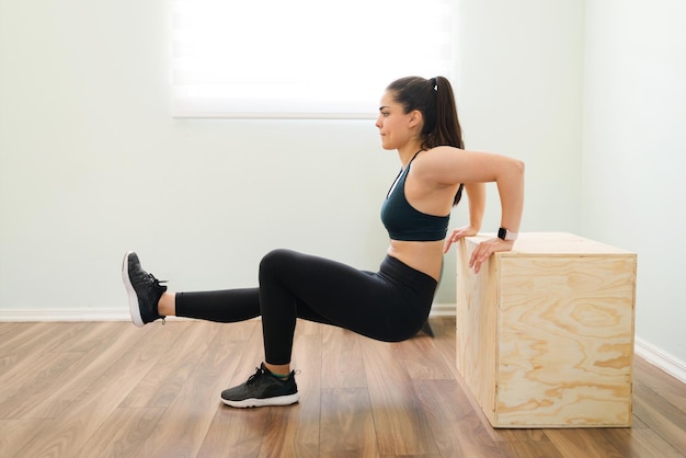 Perfil de una hermosa mujer activa de unos 30 años usando ropa deportiva negra y haciendo inmersiones de tríceps con una caja de salto