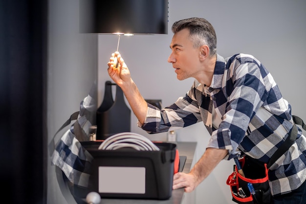 Perfil de renovación del hombre concentrado que toca el destornillador a la lámpara en la campana extractora de la cocina