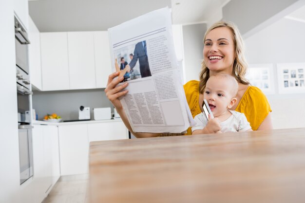 Periódico de la lectura de la madre con el bebé en la cocina