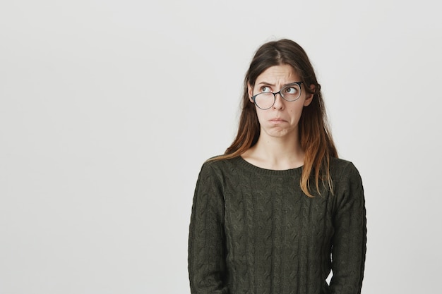 Perpleja y perpleja joven con gafas torcidas mirando a la izquierda preocupado