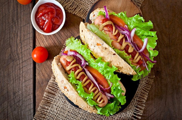 Perrito caliente con salsa de tomate mostaza y lechuga en la mesa de madera.