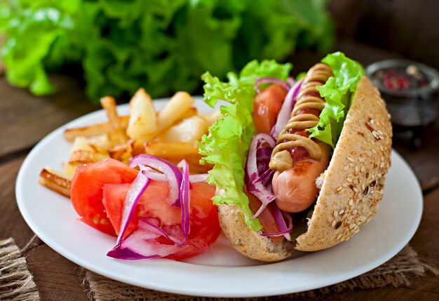 Perrito caliente con salsa de tomate mostaza y lechuga en la mesa de madera.