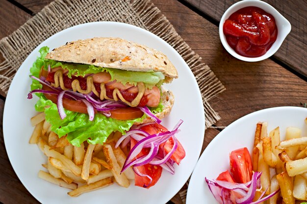 Perrito caliente con salsa de tomate mostaza y lechuga en la mesa de madera.