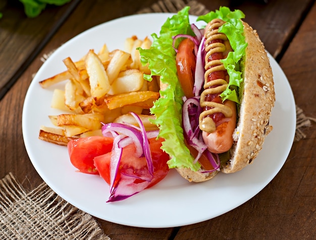 Perrito caliente con salsa de tomate mostaza y lechuga en la mesa de madera.