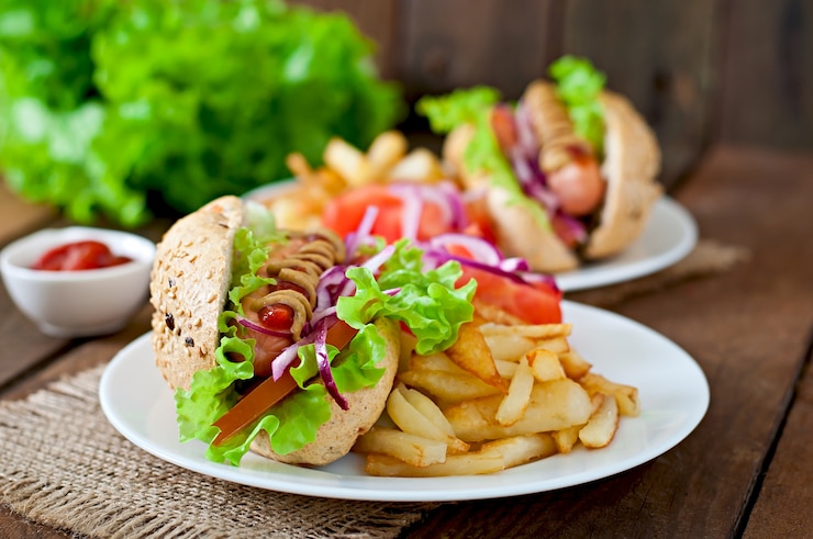 Foto gratuito perrito caliente con salsa de tomate mostaza y lechuga en la mesa de madera.