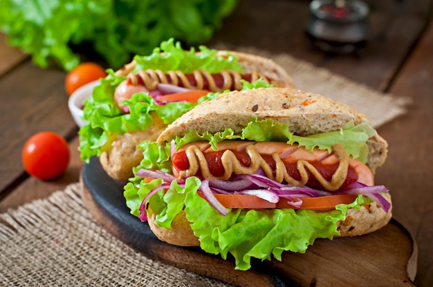 Perrito caliente con salsa de tomate mostaza y lechuga en la mesa de madera.