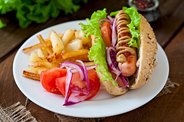 Perrito caliente con salsa de tomate mostaza y lechuga en la mesa de madera.