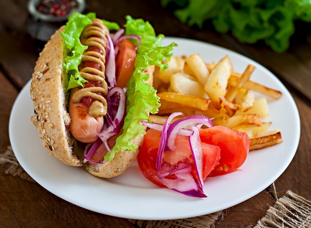 Perrito caliente con salsa de tomate mostaza y lechuga en la mesa de madera.