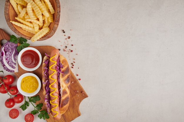 Perrito caliente de ternera a la parrilla gourmet con acompañamientos y papas fritas. Deliciosos y sencillos hot dogs con mostaza, pimiento, cebolla y nachos. Perritos calientes completamente cargados con ingredientes variados en una tabla de remo.