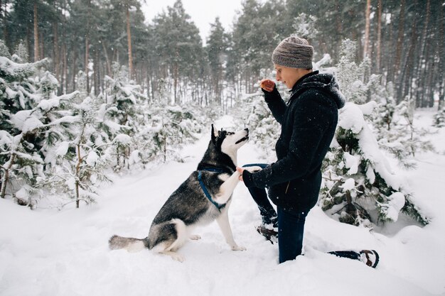 Perro de entrenamiento Hombre para entrenar a perro Husky en el bosque de invierno cubierto de nieve en el frío día de invierno
