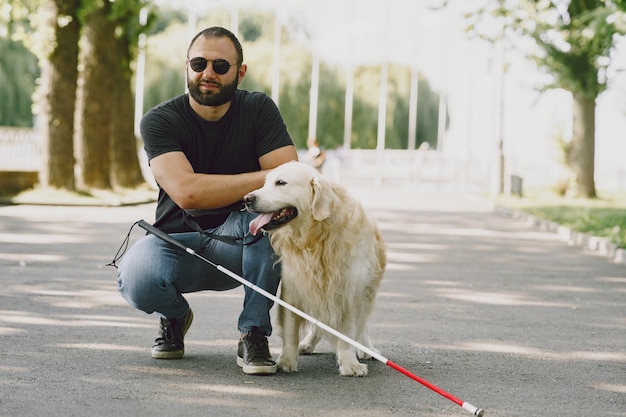 Perro guía ayudando a ciego en la ciudad. Chico ciego guapo tiene descanso con golden retriever en la ciudad.