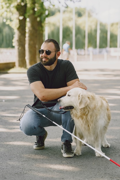 Foto gratuita perro guía ayudando a ciego en la ciudad. chico ciego guapo tiene descanso con golden retriever en la ciudad.