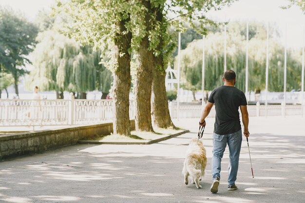 Perro guía ayudando a ciego en la ciudad. Chico ciego guapo tiene descanso con golden retriever en la ciudad.