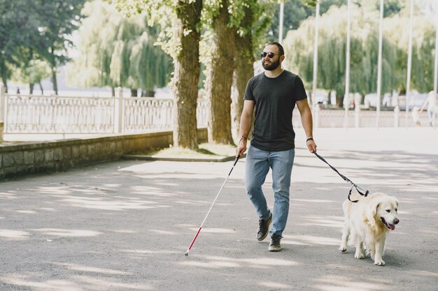 Perro guía ayudando a ciego en la ciudad. Chico ciego guapo tiene descanso con golden retriever en la ciudad.