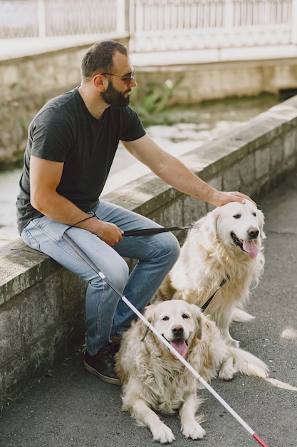 Perro guía ayudando a ciego en la ciudad. Chico ciego guapo tiene descanso con golden retriever en la ciudad.