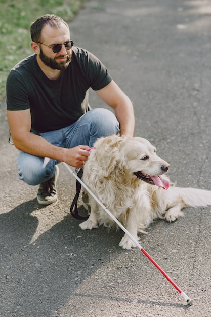 Perro guía ayudando a ciego en la ciudad. Chico ciego guapo tiene descanso con golden retriever en la ciudad.