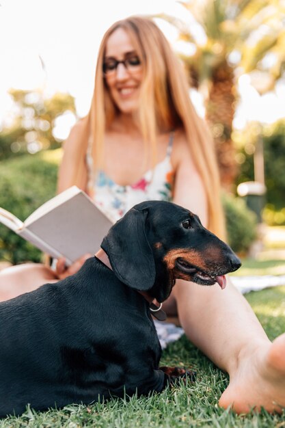 Perro sentado delante de libro de lectura sonriente de mujer joven