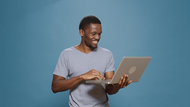 Persona alegre navegando por Internet en una computadora portátil en el estudio, usando una PC electrónica portátil para navegar en las redes sociales y en la red de sitios web en línea. Hombre feliz sosteniendo un aparato inalámbrico.