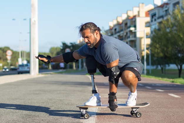 Persona atractiva con discapacidad haciendo deportes en el parque. Deportista adulto medio andando en monopatín por un camino especial en concentración. Deporte, discapacidad, concepto de entrenamiento.