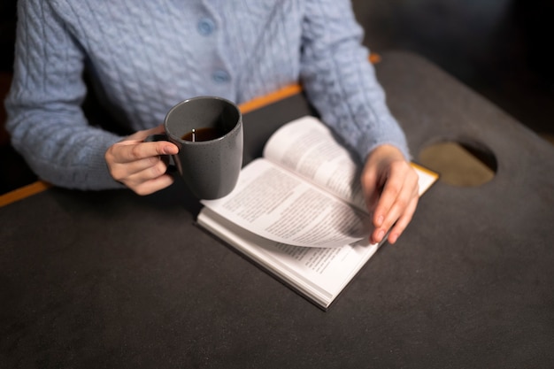 Foto gratuita persona en un café leyendo un libro mientras toma un café